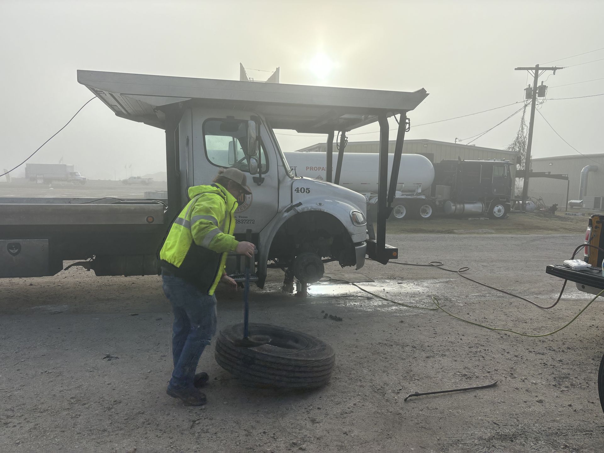A person changing a tire on a tow truck on a foggy day.