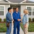 Two technicians in blue uniforms greeting a homeowner outside a house