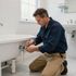 Plumber tightening a sink pipe under a bathroom tub in a bright white bathroom