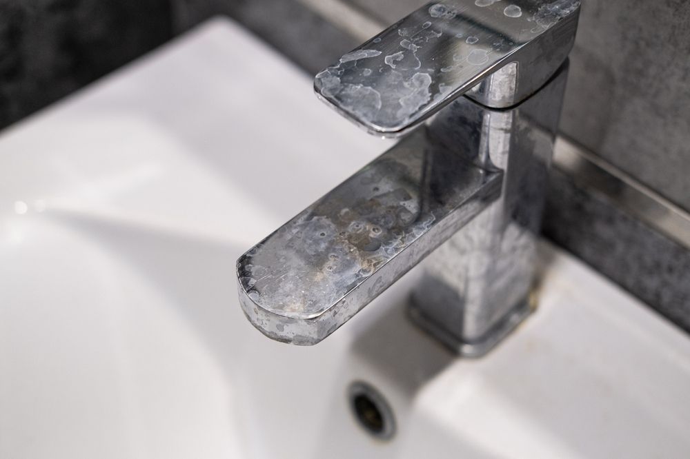 Close-up of a chrome bathroom faucet over a white sink with water spots