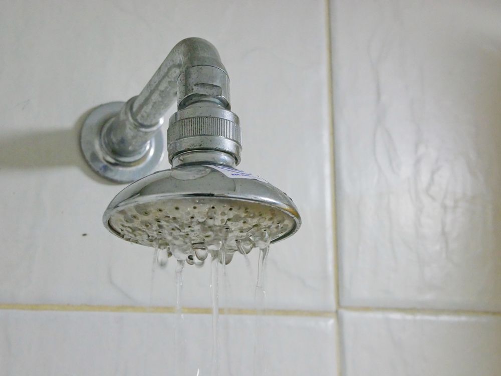 Chrome showerhead mounted on a white tiled bathroom wall, with water nozzles visible