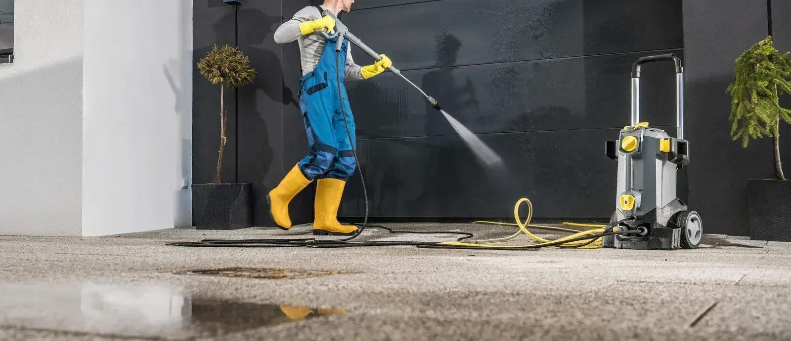 A person is using a high pressure washer to clean a wooden deck.