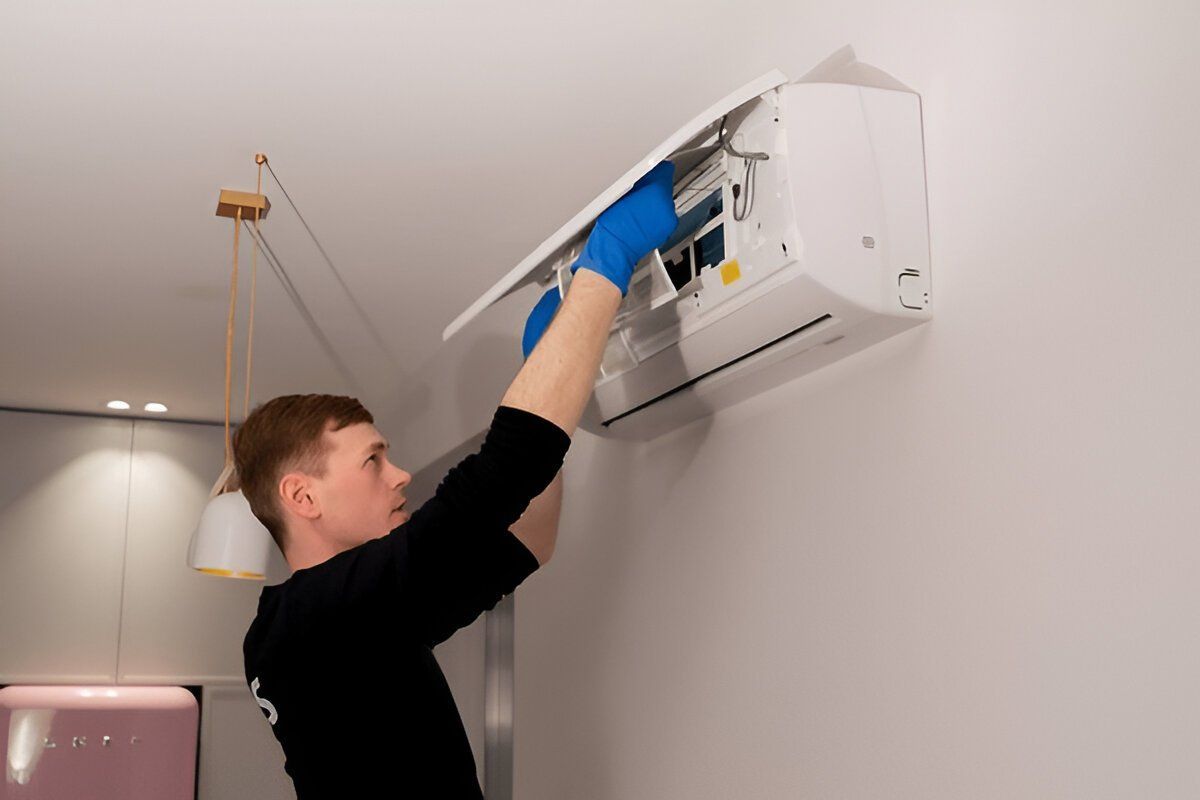 A man is cleaning an air conditioner on a wall.