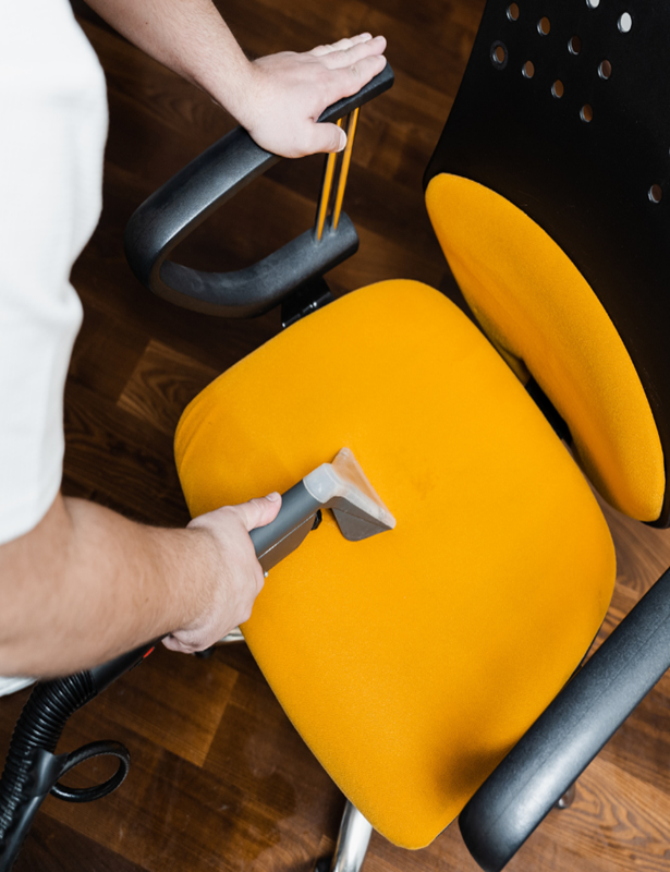 A person is cleaning a yellow chair with a vacuum cleaner