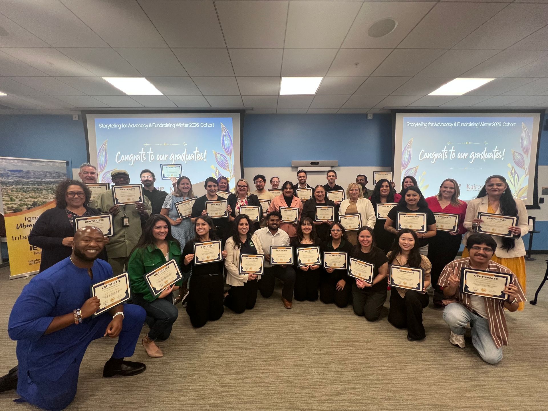 Group of people holding certificates in a classroom, posing in front of a projection screen.