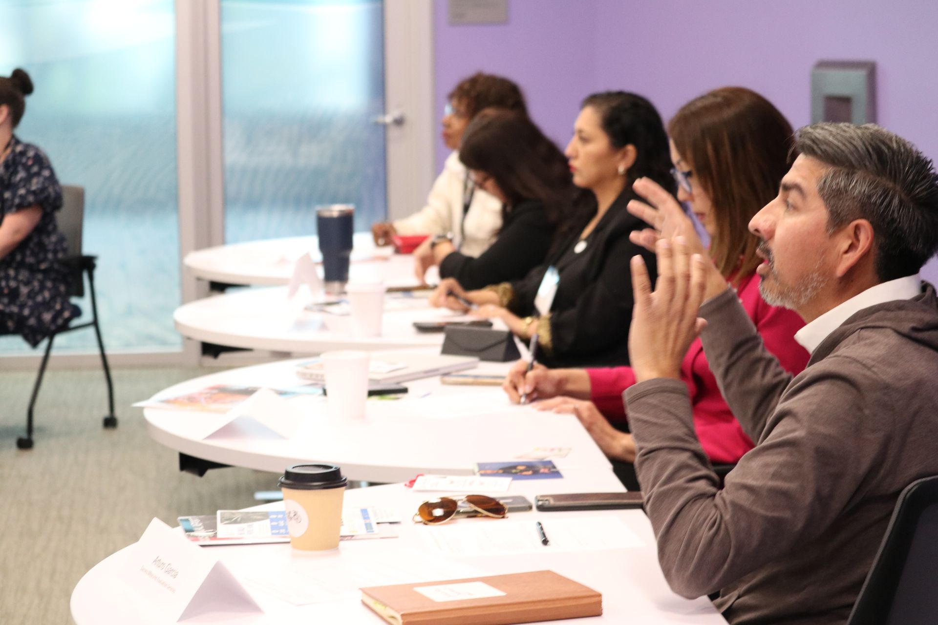 People seated at a conference table, listening and taking notes during a meeting
