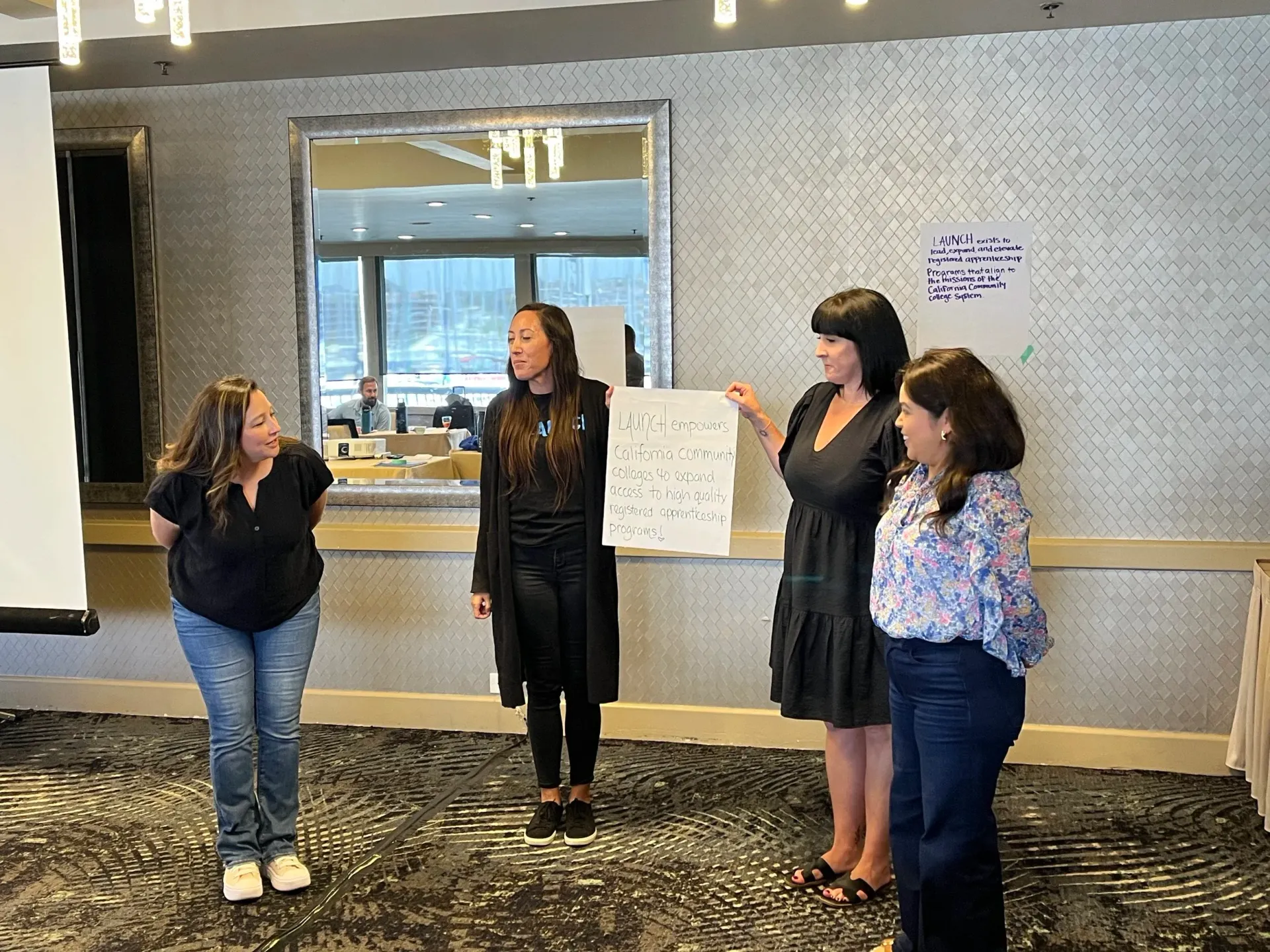 Four people present a sign in a meeting room, two women are holding it.