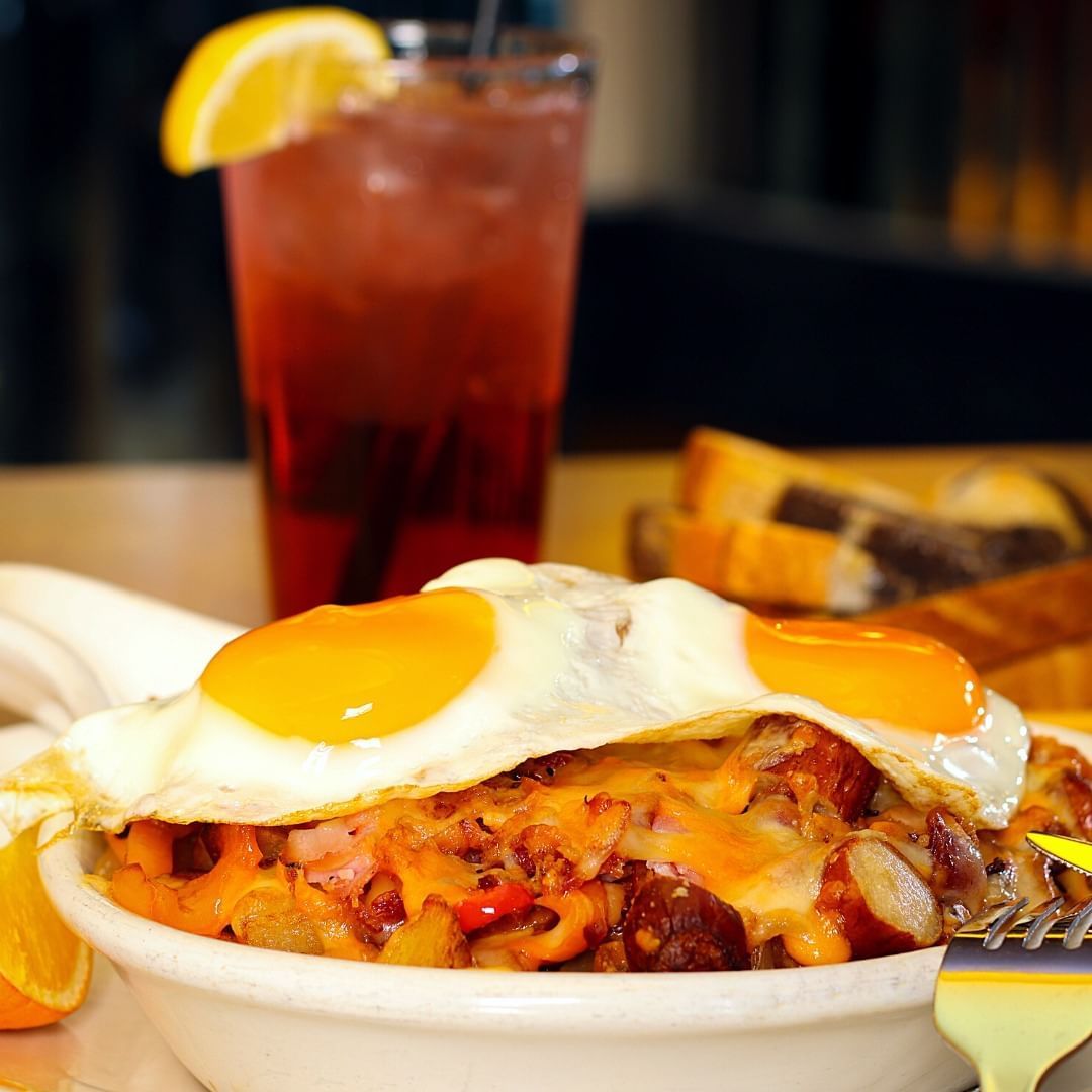 A bowl of food with a fried egg on top and a drink in the background.