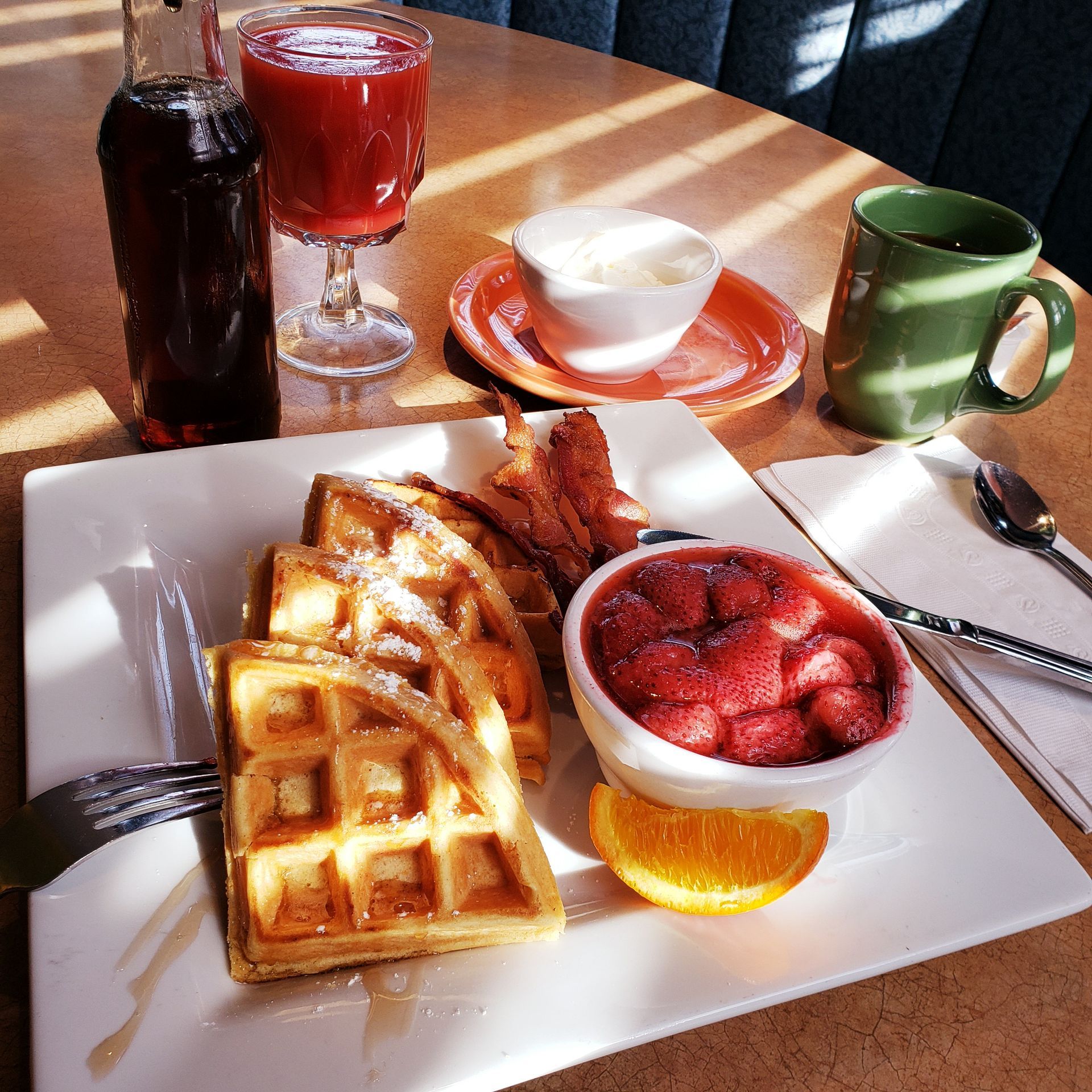 A white plate topped with waffles bacon and strawberries