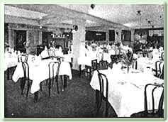 A black and white photo of a restaurant filled with tables and chairs.