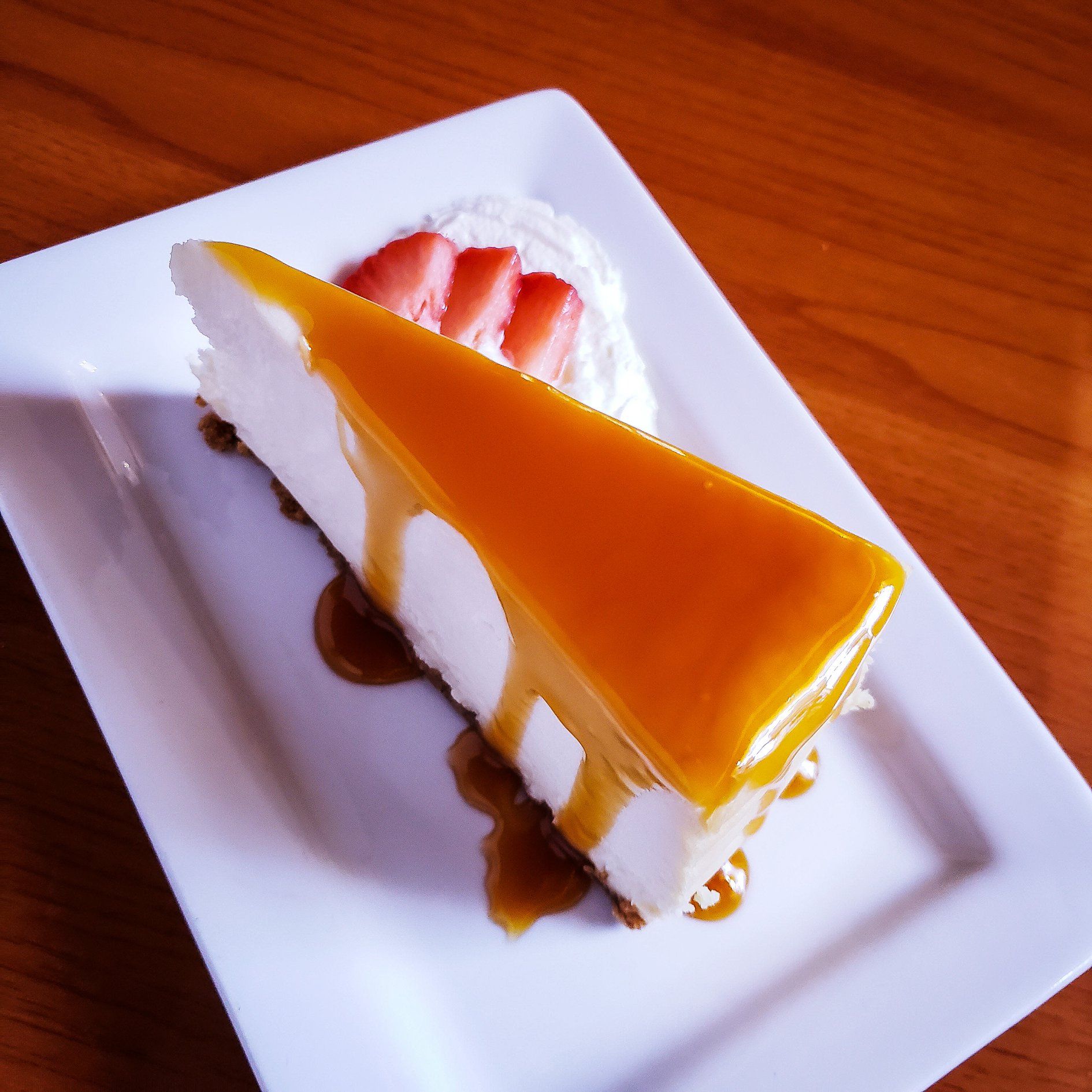 A slice of cheesecake on a white plate with whipped cream and strawberries