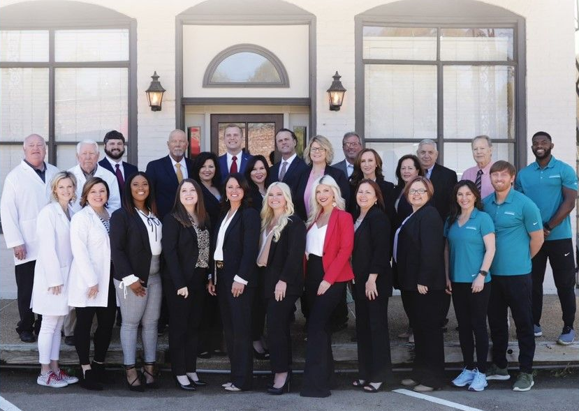 Group of people posing outside a building with white and dark colored attire.