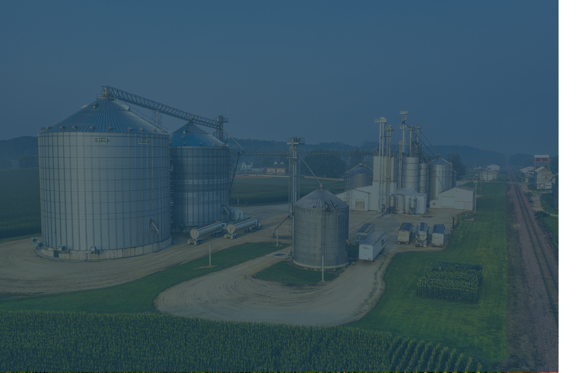 Large grain storage facility in a rural setting. Blue sky, silos, and conveyors.