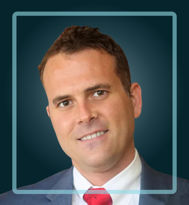 Man in a suit smiling, red tie, blue suit jacket, light skin, framed in blue on a blue gradient background.