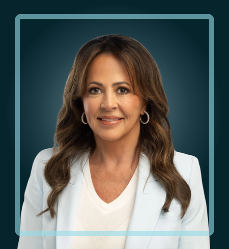 Woman with brown hair smiles, wearing a light blue blazer and hoop earrings, against a teal background.