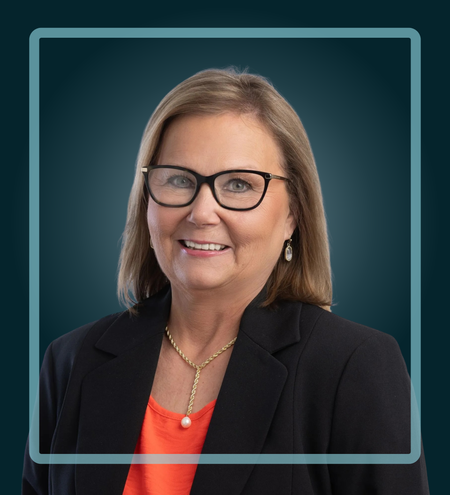 Woman wearing glasses, smiling, with a gold necklace and a dark blazer.