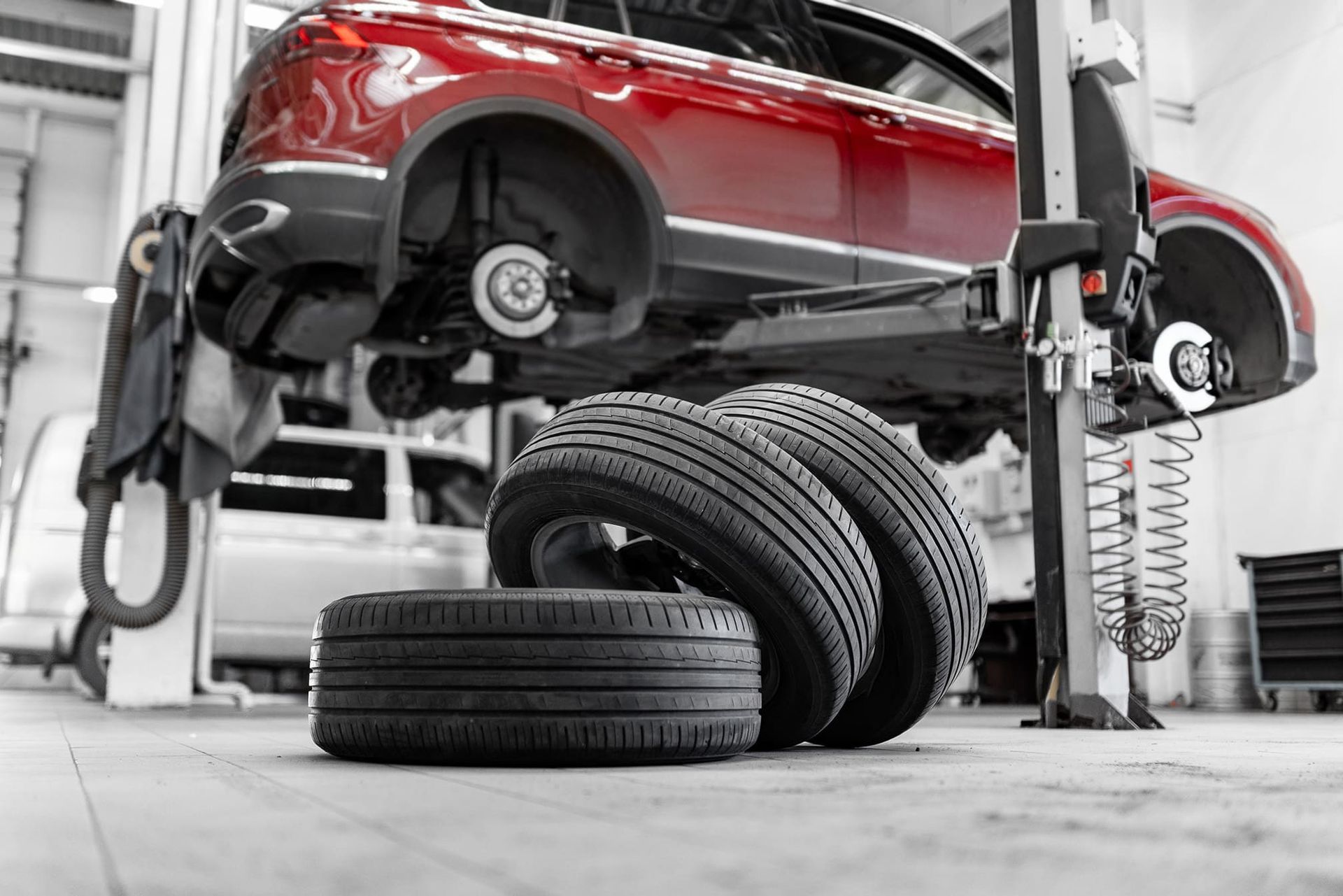 Red car on a lift in a garage, tires stacked on the floor.