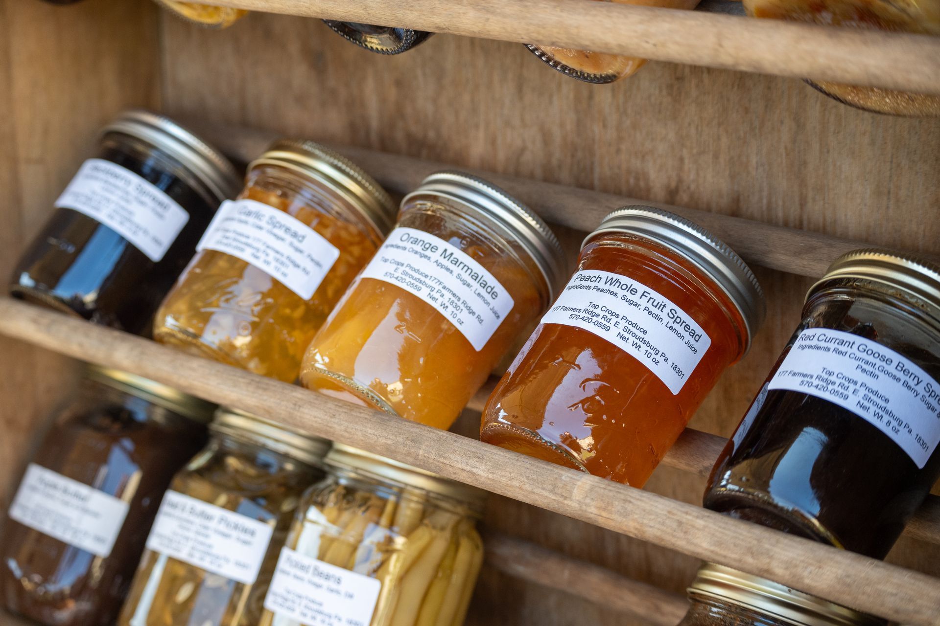 Jars of jam are lined up on a wooden shelf.
