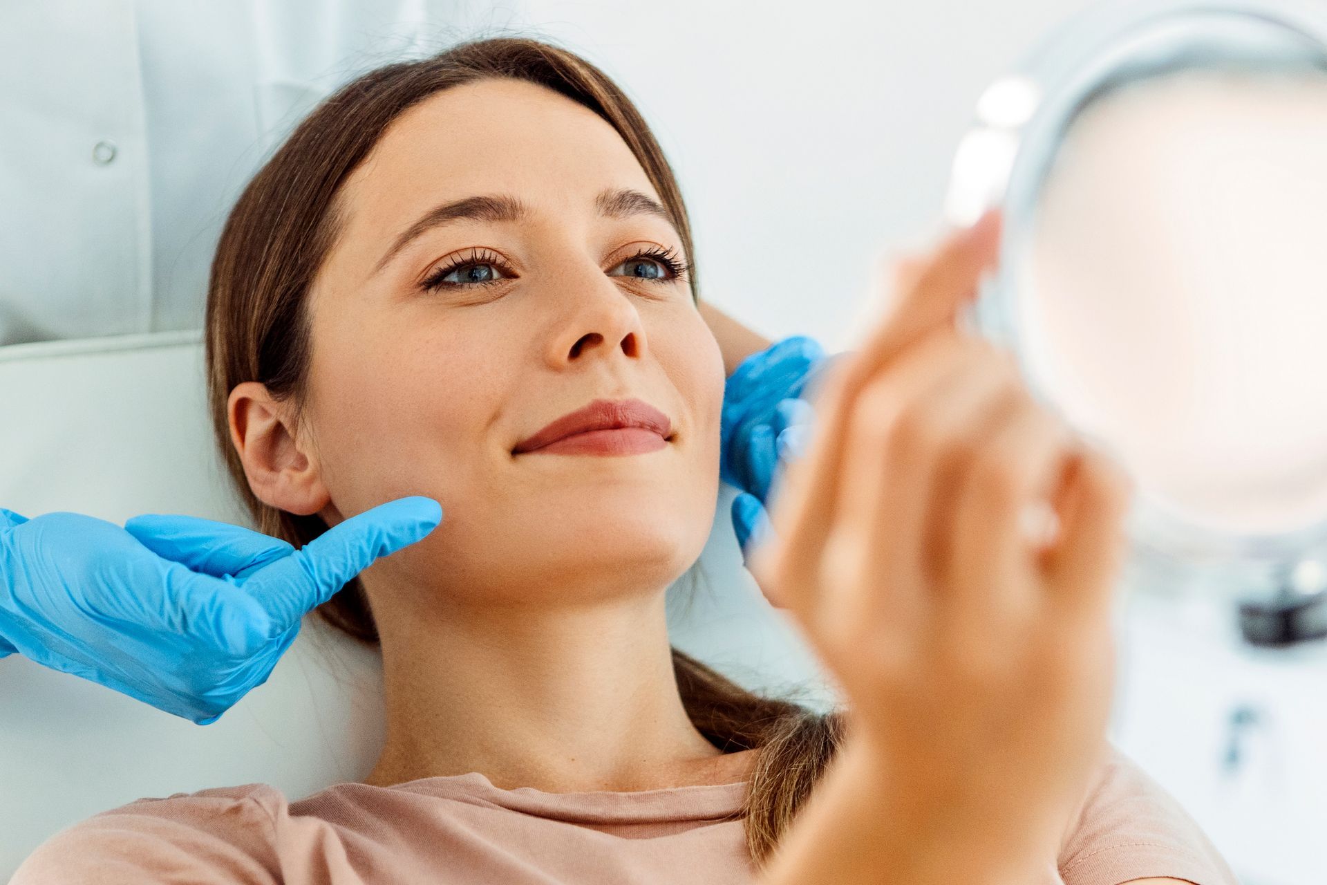 A woman looking at a mirror and smiling after a hair removal treatment with a medical professional.