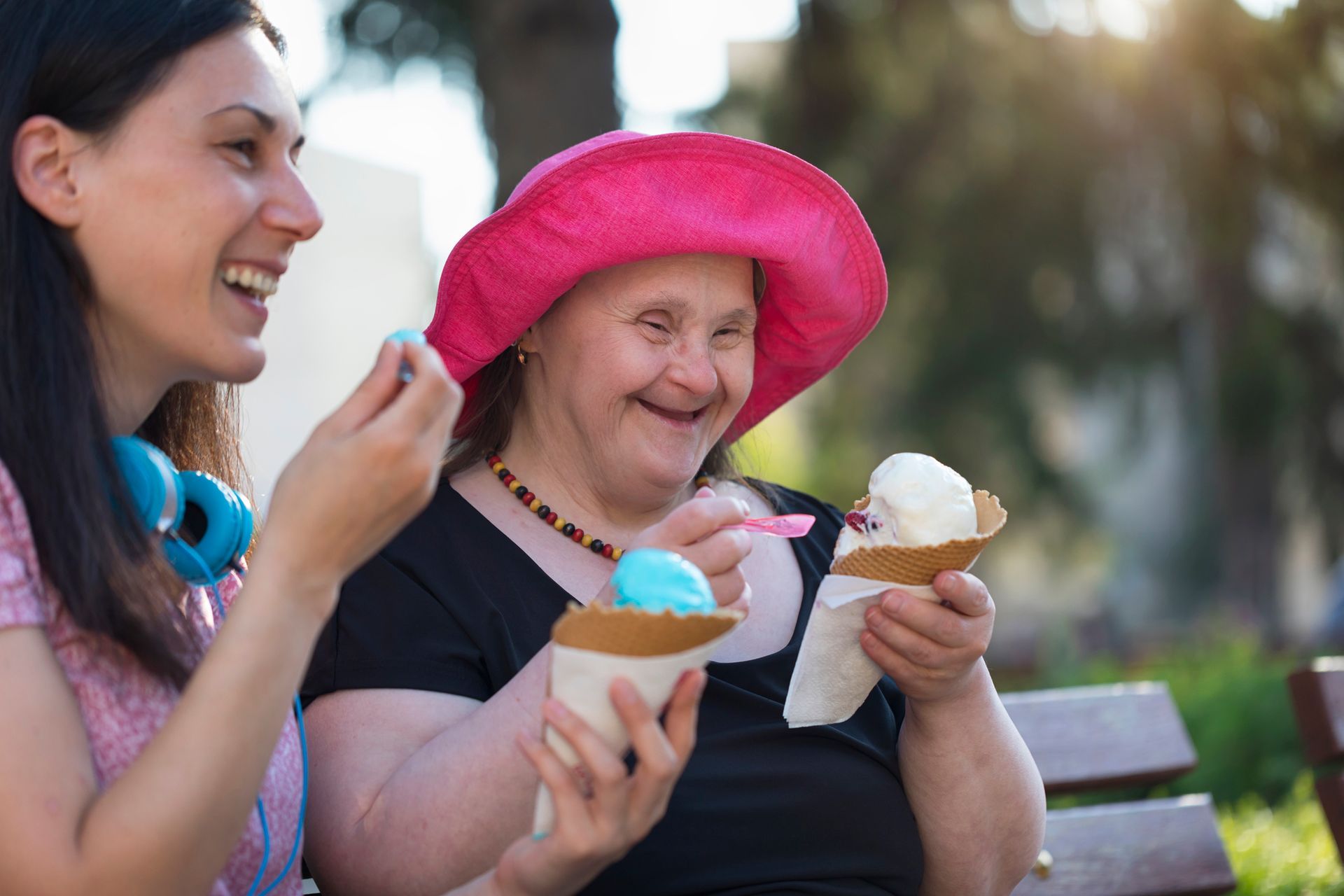 A woman and a woman with down syndrome are eating ice cream on a bench.