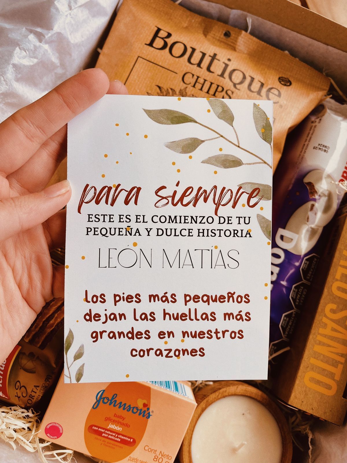 Una caja llena de un babero, un chupete, jabón y dulces.