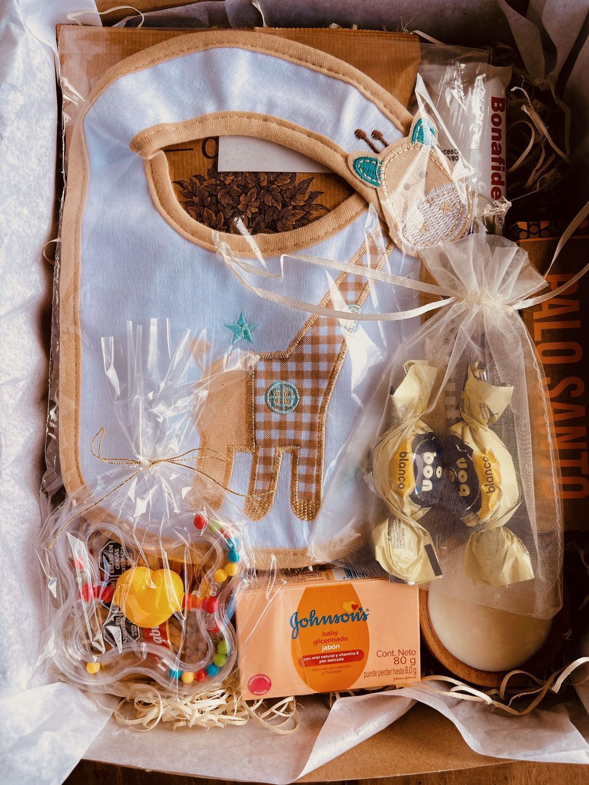 Una caja llena de un babero, un chupete, jabón y dulces.
