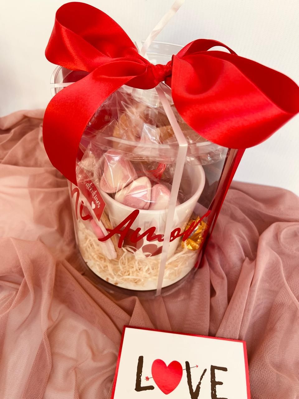 Un recipiente transparente con un lazo rojo y una tarjeta que dice amor.