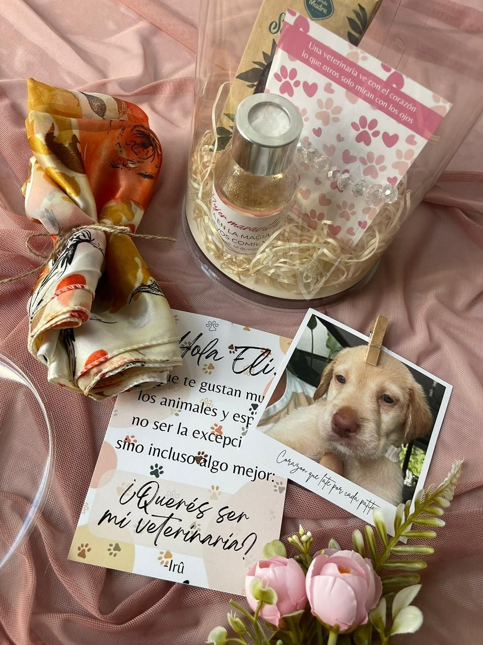 Un cachorro está sentado en una mesa junto a una tarjeta y flores.