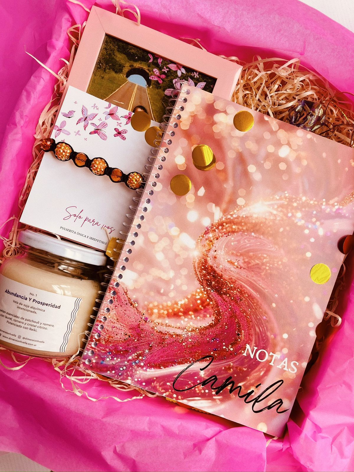 Una caja rosa llena de un cuaderno, una vela y una pulsera.