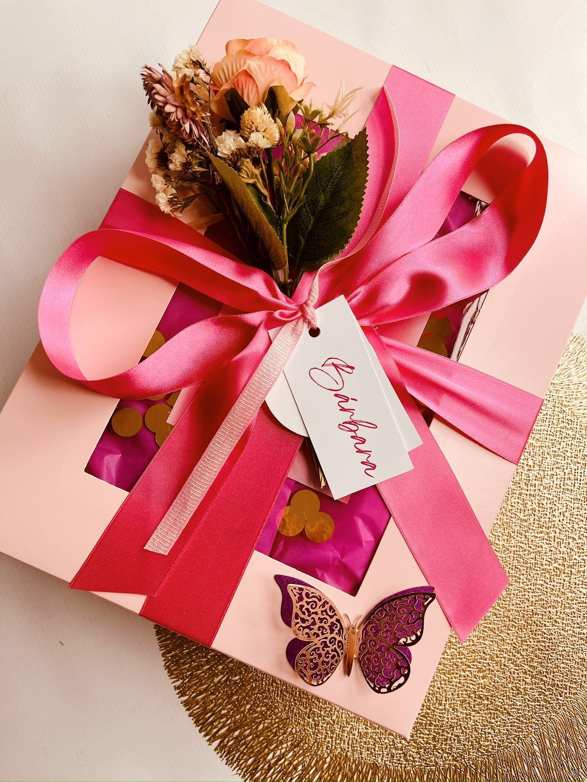Una caja de regalo rosa con flores y una mariposa.