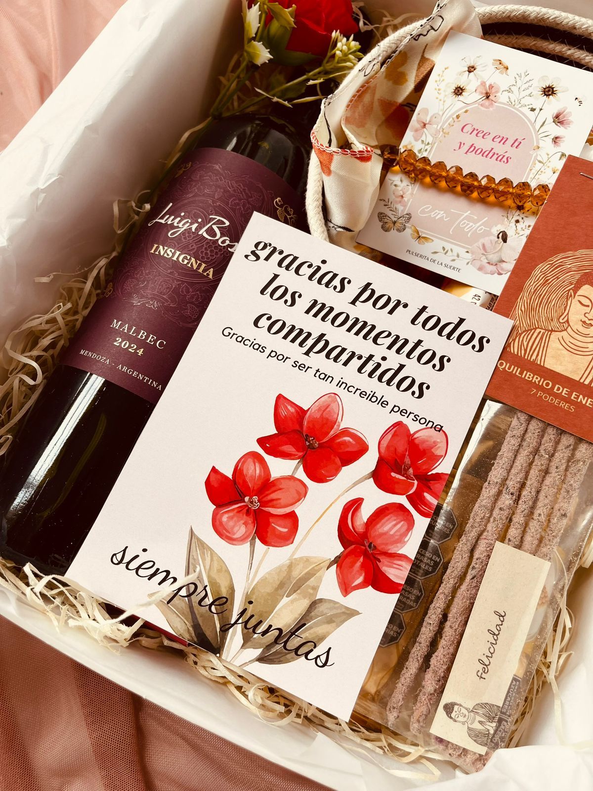 Una caja llena de una botella de vino, un cuenco, un cuadro y varitas de incienso.