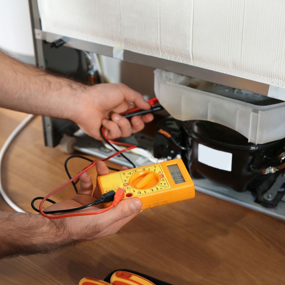 A man is working on a refrigerator with a multimeter
