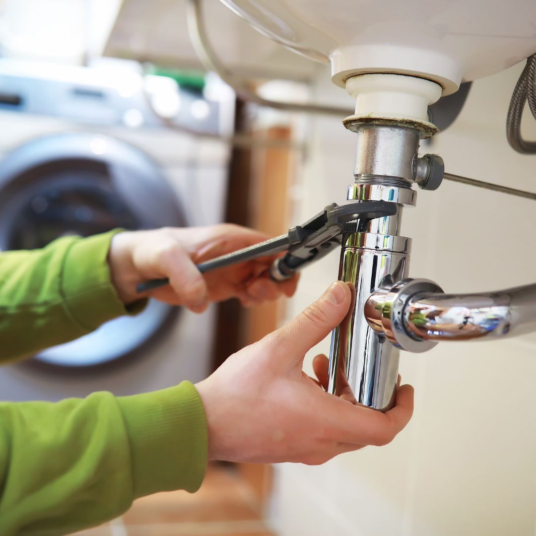 A person is fixing a sink with a wrench