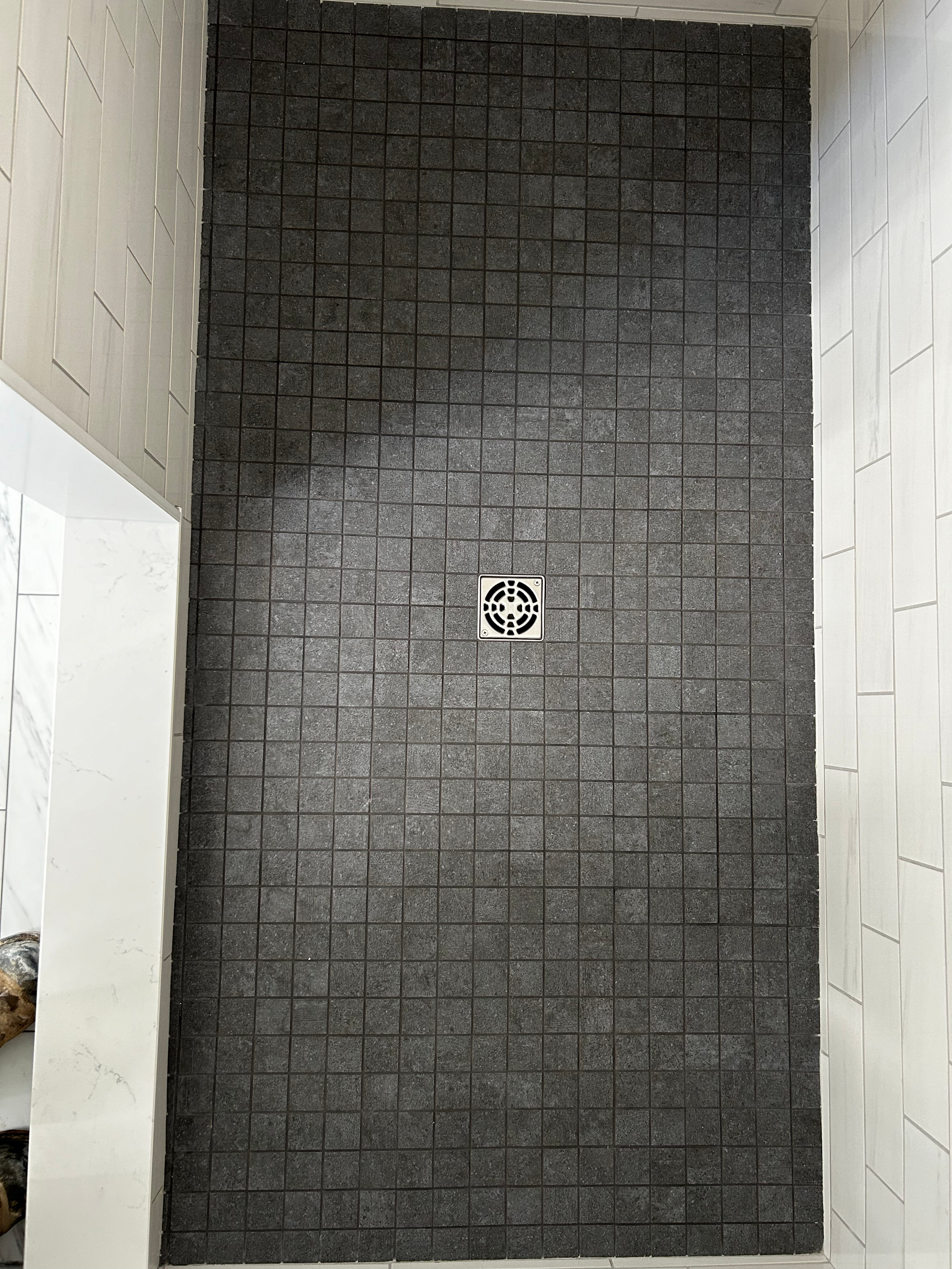 A shower stall with a black tile wall and a drain.