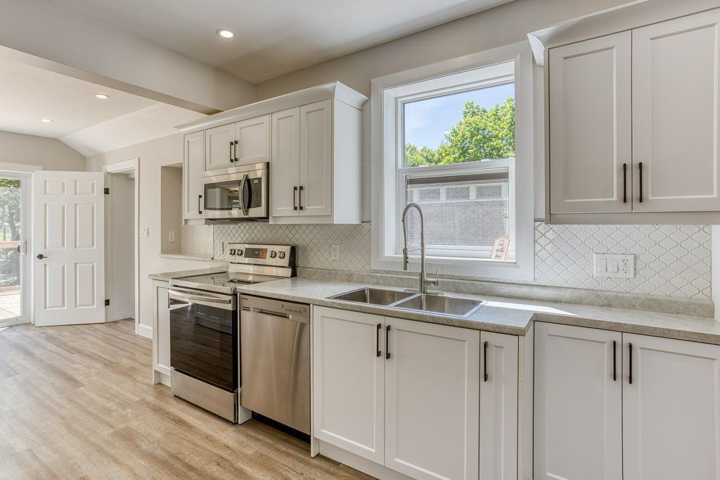 A kitchen with white cabinets , stainless steel appliances , a sink , and a window.