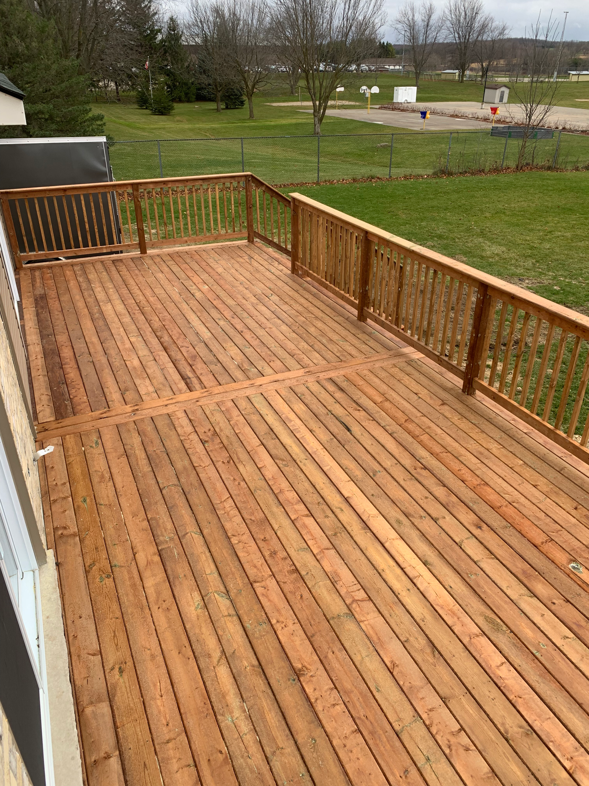 A large wooden deck with a fence and a view of a field.