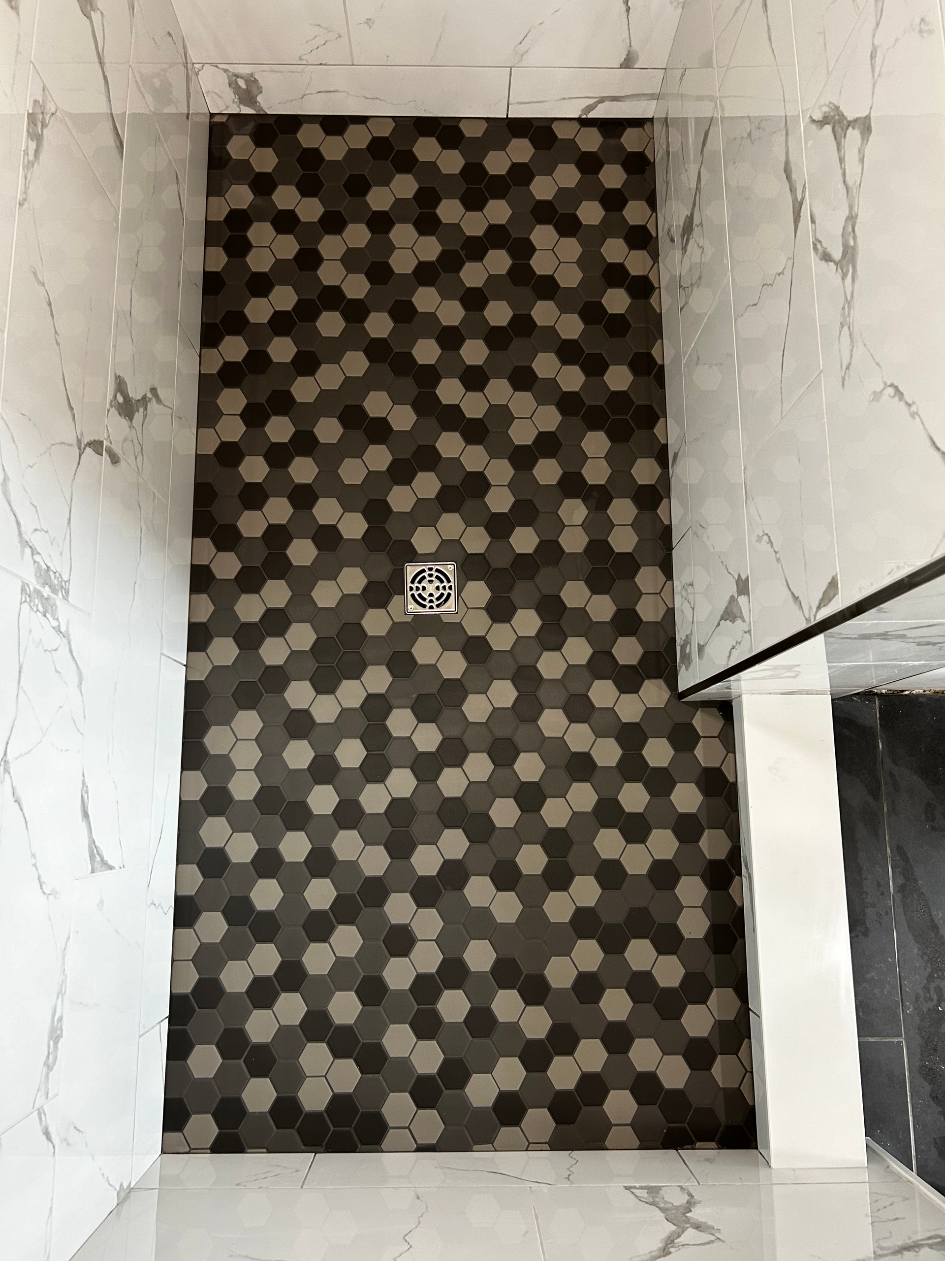 A shower stall with a hexagonal tile floor and a drain.