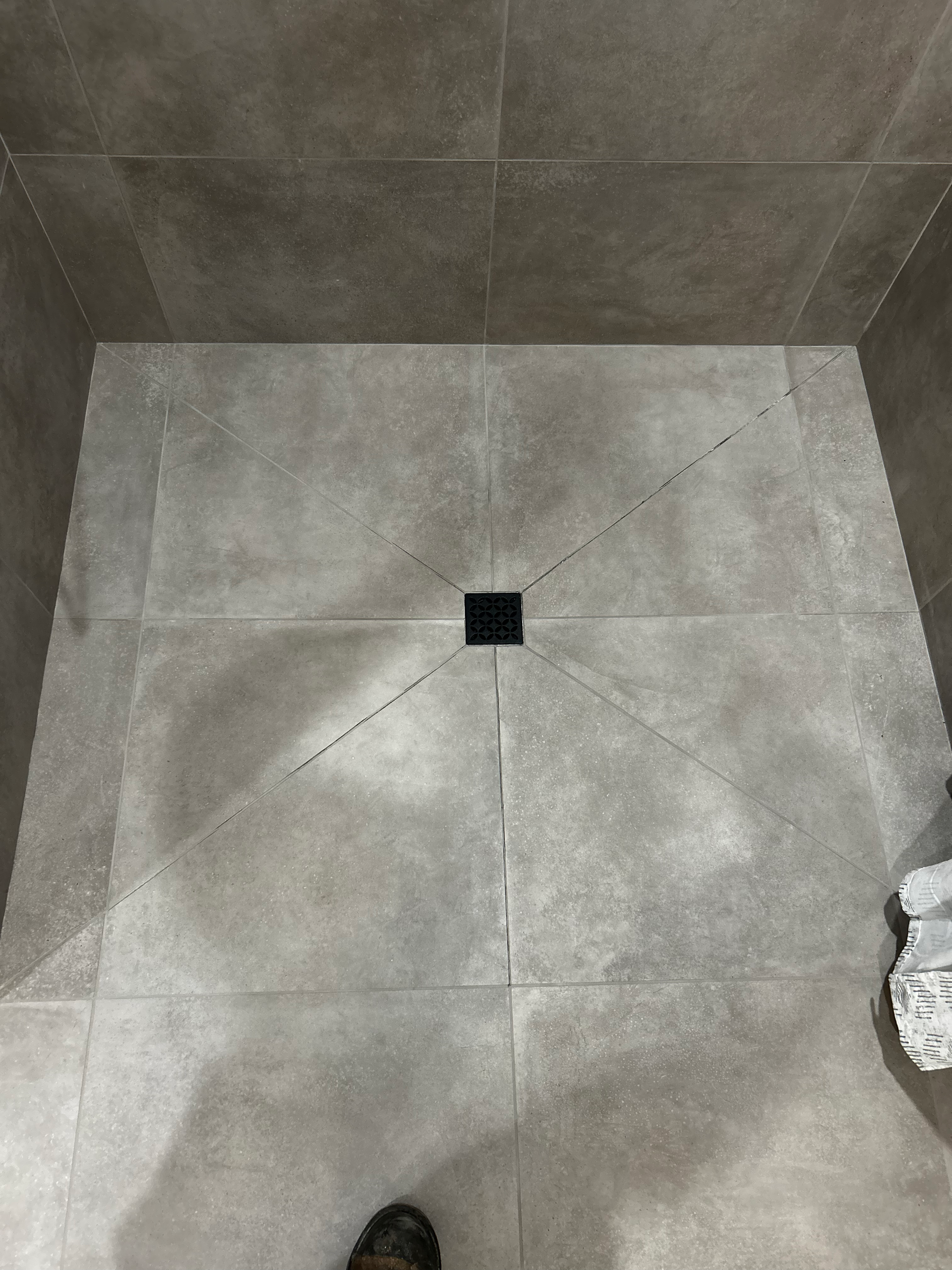 A person is standing in a shower with a drain in the floor.