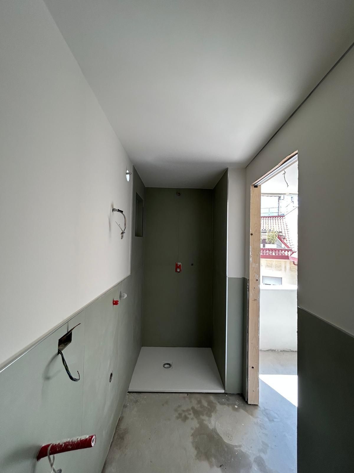 Bagno in costruzione: pareti grigie e bianche, piatto doccia, porta aperta sulla luce.