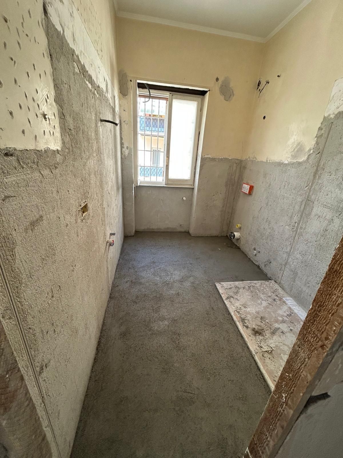 Stanza in costruzione con pareti e pavimento in cemento, piccola finestra.