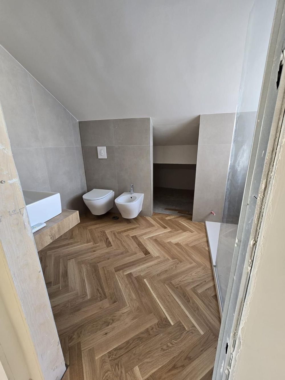 Bagno con pavimento in legno a spina di pesce, pareti piastrellate beige, WC, bidet.