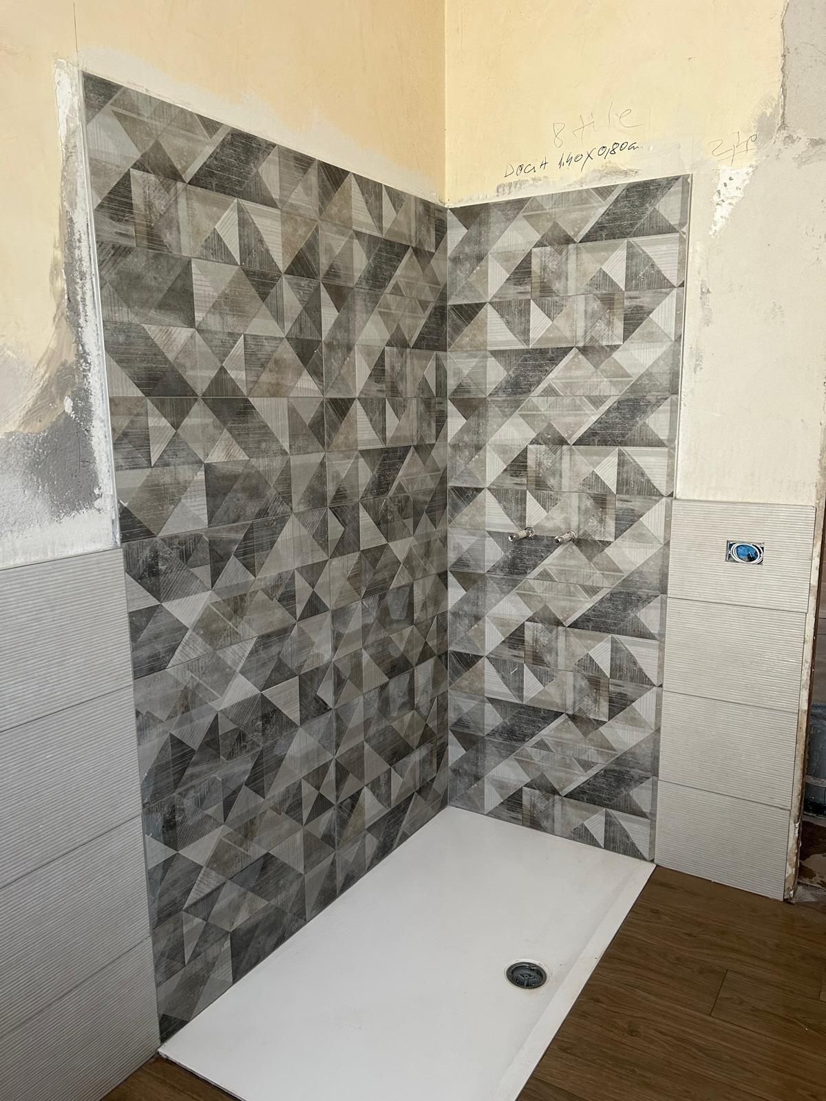 Box doccia con piastrelle geometriche grigie e base bianca.