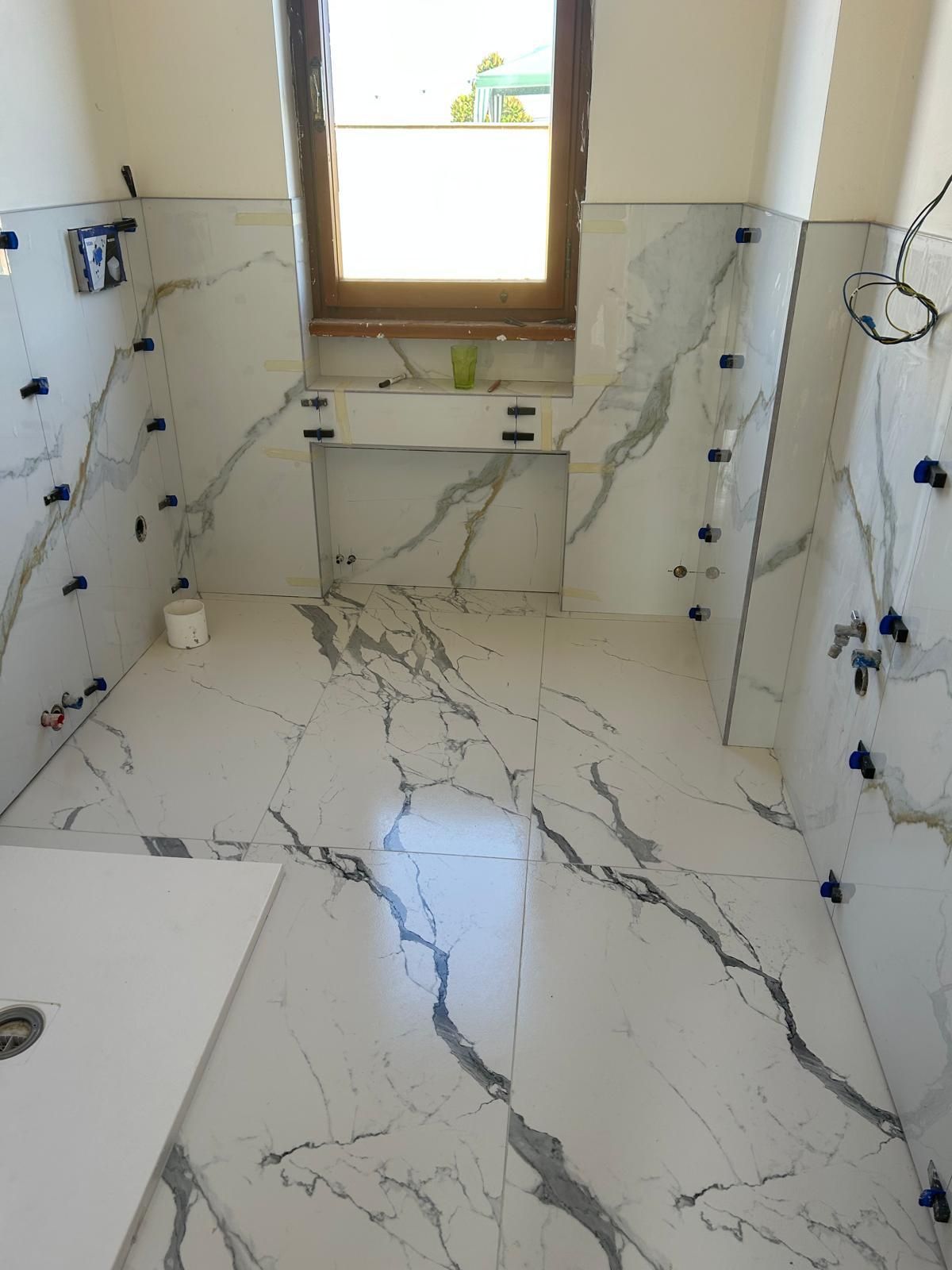 Bagno con pavimento e pareti rivestiti in piastrelle di marmo bianco. Sono visibili una finestra e un lavandino.