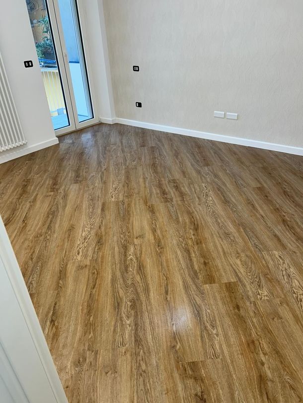Camera con pavimento in legno, pareti dai colori chiari e una grande porta a vetri; è visibile un termosifone.