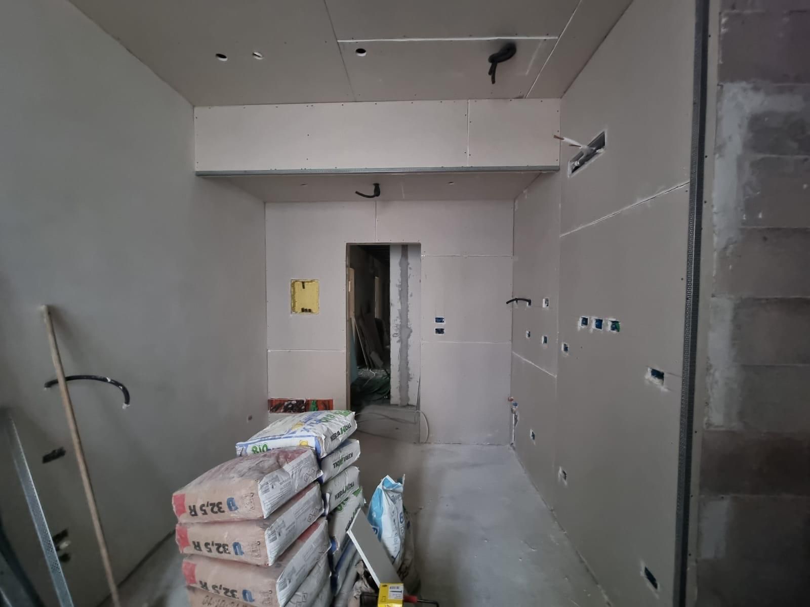 Cantiere: pareti in cartongesso, sacchi di cemento, porta che conduce a un'altra stanza.