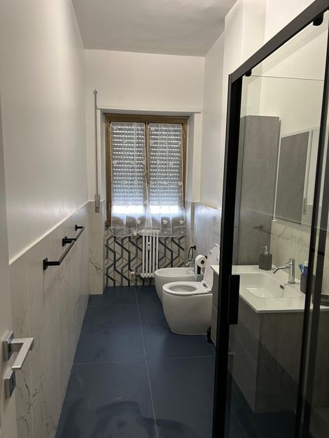 Bagno moderno e stretto con pavimento blu, pareti bianche e doccia in vetro.