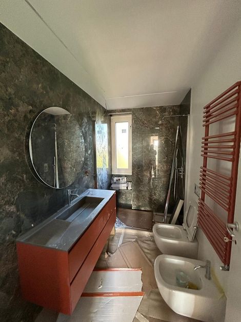 Bagno moderno in costruzione: mobile lavabo rosso, parete testurizzata grigio scuro e portasciugamani rosso.