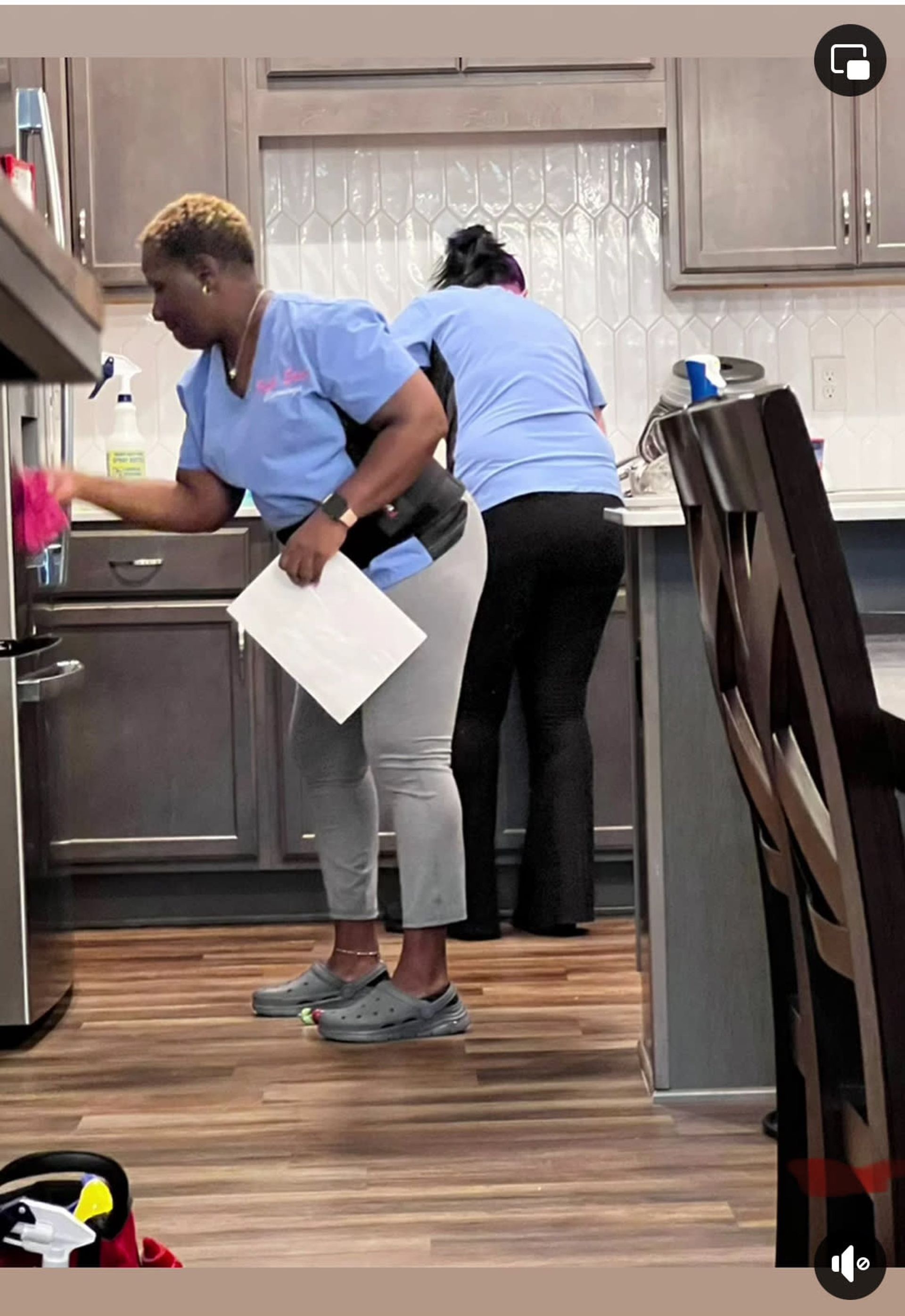 Two women are cleaning a kitchen and one is holding a piece of paper.