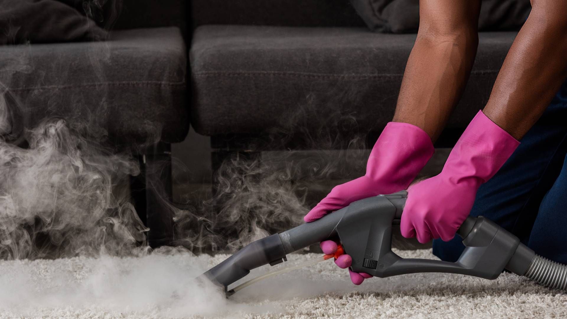 A person wearing pink gloves is using a vacuum cleaner to clean a carpet.