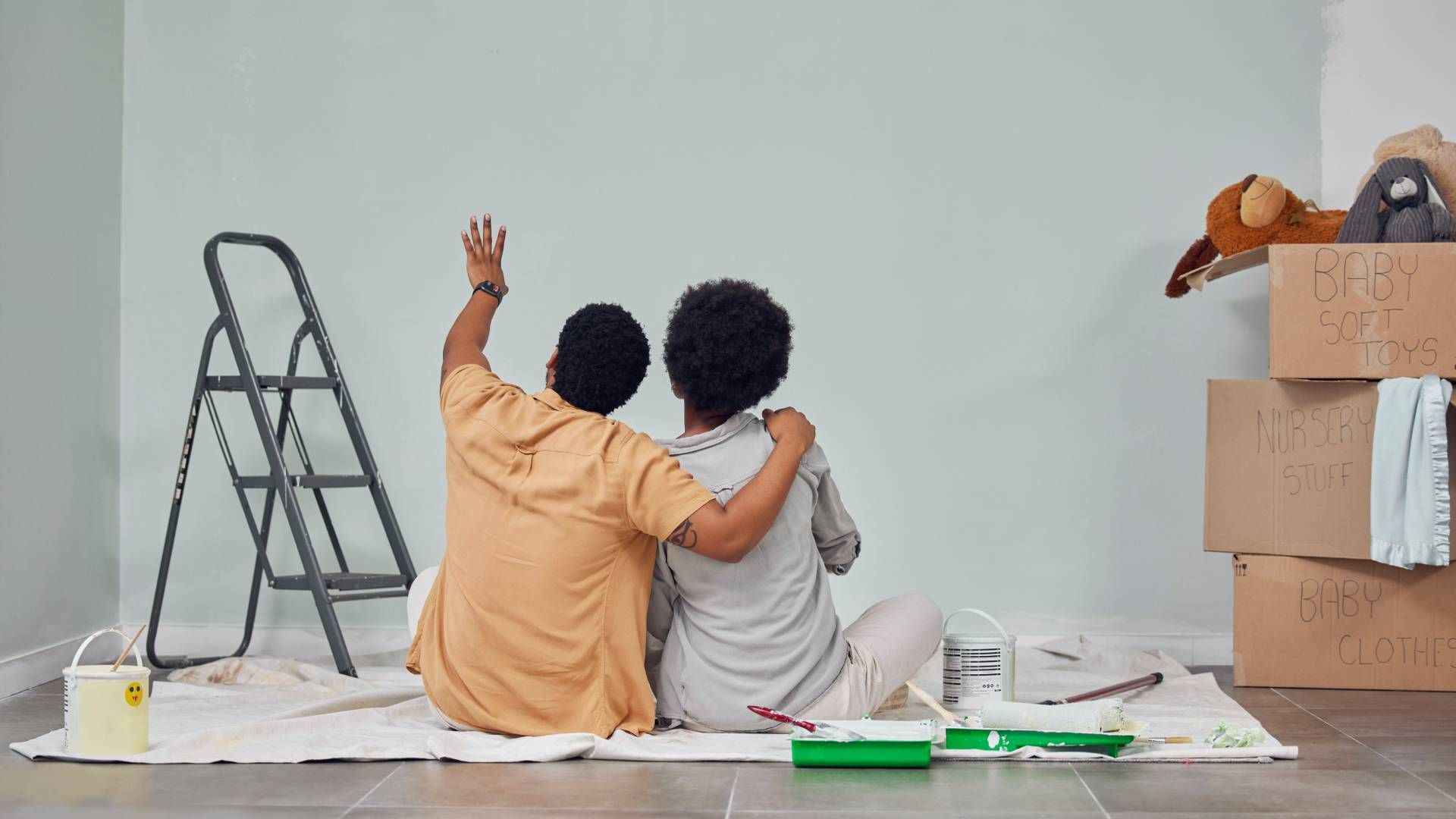 Two people are sitting on the floor looking at a wall.